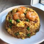 A mound of savory shrimp fried rice topped with three large cooked shrimp and mixed with bright green peas and scrambled egg.
