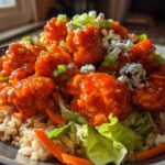 A close-up of a delicious buffalo chicken bowl featuring saucy chicken, brown rice, lettuce, carrots, and blue cheese crumbles.