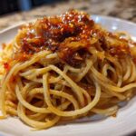 A close-up of spaghetti tossed in sauce and topped with rich caramelized onion pasta mixture.