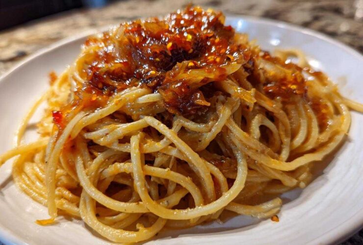 A close-up of spaghetti tossed in sauce and topped with rich caramelized onion pasta mixture.