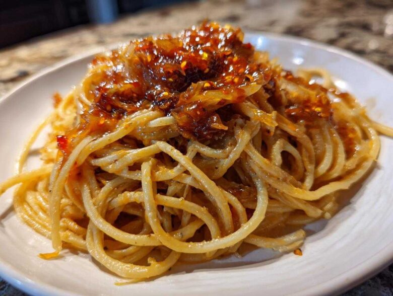 A close-up of spaghetti tossed in sauce and topped with rich caramelized onion pasta mixture.