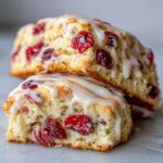 Two flaky cranberry orange scones stacked, drizzled with a sweet white glaze and filled with dried cranberries.