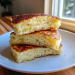 Close-up of three thick, fluffy almond flour pancakes stacked on a white plate, showing the airy interior.