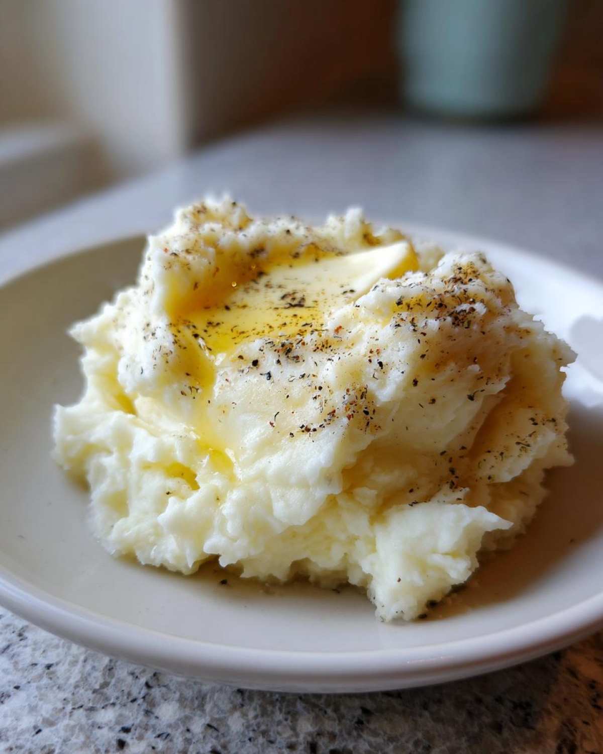 A close-up of fluffy slow cooker mashed potatoes topped with melting butter and cracked black pepper.
