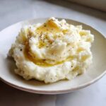 A serving of fluffy slow cooker mashed potatoes topped with melted butter and cracked black pepper.