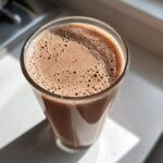 Close-up overhead view of a glass filled with freshly made, frothy chocolate milk sitting in bright sunlight.