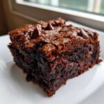 A close-up of a fudgy, dark chocolate date brownies square topped with melted chocolate chips.