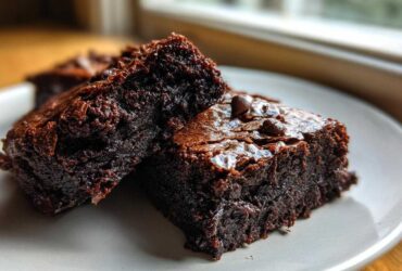 Two fudgy date brownies stacked slightly, showing a rich, dark interior and shiny top with chocolate chips.