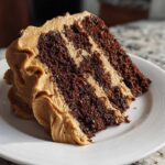 A close-up of a rich slice of gingerbread latte cake showing dark chocolate layers alternating with light brown coffee frosting.