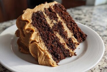 A close-up of a rich slice of gingerbread latte cake showing dark chocolate layers alternating with light brown coffee frosting.