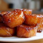 A stack of beautifully glazed candied sweet potatoes glistening with syrup on a white plate.