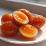 Close-up of glossy, orange-colored marinated eggs, some whole and some halved showing jammy yolks.