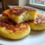 Close-up of four golden brown, pan-fried Irish potato farls stacked on a white plate, one piece broken open showing the fluffy interior.