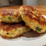 Three perfectly pan-fried mashed potato cakes, golden brown and speckled with green onions, stacked on a white plate.