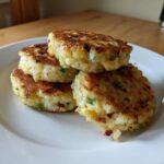 A stack of four golden brown, pan-fried mashed potato cakes with visible green onions and bacon bits.