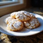 A stack of freshly baked, crinkled gooey butter cookies generously dusted with powdered sugar on a white plate.