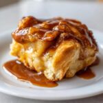 A single, warm apple dumpling smothered in rich caramel sauce, sitting on a white plate.
