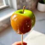 Close-up of a Granny Smith apple partially dipped in glossy, rich caramel, ready to eat as a caramel apples treat.