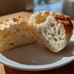 Close-up of homemade English muffins split in half showing the signature open, airy crumb structure.