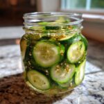 Close-up of sliced cucumbers packed tightly in a glass jar for refrigerator pickles, seasoned with dill and mustard seeds.