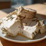 Slices of juicy crockpot turkey breast seasoned with rosemary and garlic, resting on a white plate.