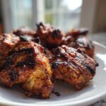 Close-up of perfectly grilled, charred chicken pieces coated in a rich red chicken marinade, served on a white plate.