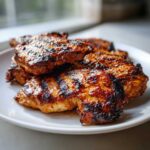 Close-up of several pieces of grilled chicken, showing char marks and a glossy coating from a flavorful chicken marinade.