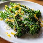 Close-up of bright green, roasted broccolini topped with grated Parmesan cheese and vibrant lemon zest.