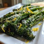 Close-up of roasted broccolini topped with grated Parmesan cheese and bright yellow lemon zest.