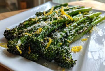 Close-up of roasted broccolini topped with grated Parmesan cheese and bright yellow lemon zest.