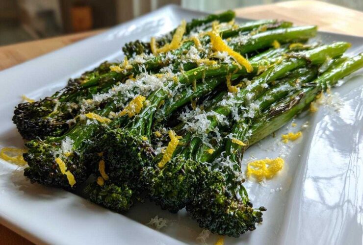 Close-up of roasted broccolini topped with grated Parmesan cheese and bright yellow lemon zest.