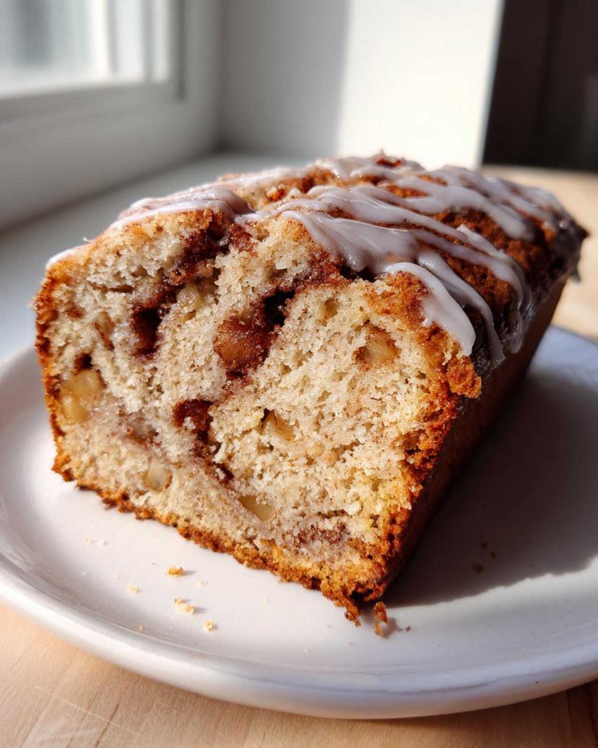 A close-up of a moist slice of apple bread featuring a cinnamon swirl and a light vanilla glaze drizzle.
