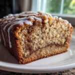 Close-up of a moist slice of apple bread with a cinnamon swirl and white vanilla glaze drizzled on top.