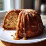 A slice removed from a moist apple bundt cake drizzled heavily with thick caramel glaze.