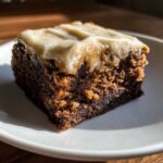 Close-up of a rich, dark banana bread brownie square topped with thick, creamy frosting.