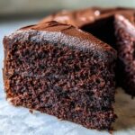 Close-up of a thick slice showing the rich, dark crumb of a moist chocolate cake topped with glossy frosting.
