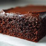 Extreme close-up of a rich, dark slice of moist chocolate cake topped with glossy chocolate frosting.