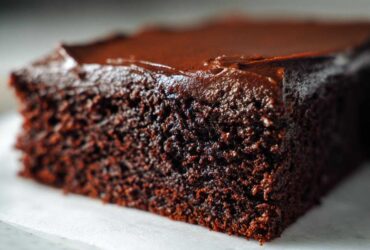 Extreme close-up of a rich, dark slice of moist chocolate cake topped with glossy chocolate frosting.
