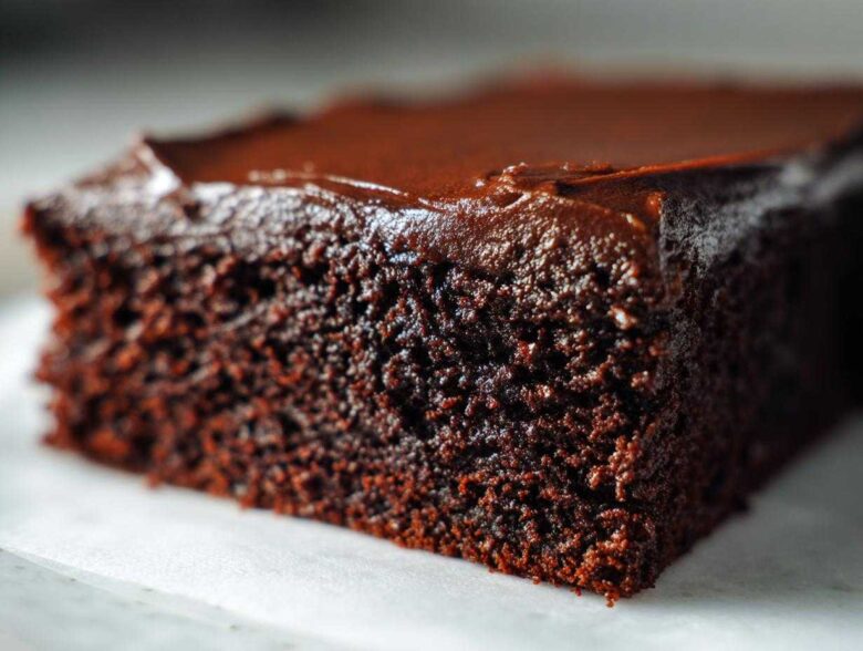 Extreme close-up of a rich, dark slice of moist chocolate cake topped with glossy chocolate frosting.