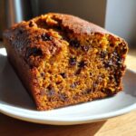 Close-up of a moist slice of chocolate chip pumpkin bread on a white plate, showing its rich orange color.