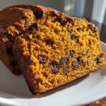 Close-up of two slices of moist pumpkin bread loaded with chocolate chips on a white plate.