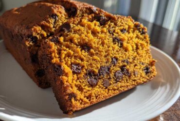 Close-up of two slices of moist pumpkin bread loaded with chocolate chips on a white plate.