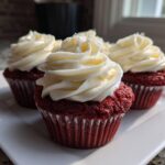 Close-up of three moist red velvet cupcakes topped with swirls of white cream cheese frosting.