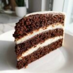 Close-up of a thick slice of dark, moist spice cake with two layers of white cream cheese frosting.