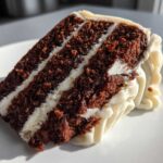 Close-up of a moist slice of three-layer spice cake with thick white frosting between layers and piped on the side.