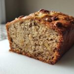 Close-up of a freshly baked loaf of sugar free banana bread, showing the moist crumb and pecan topping.