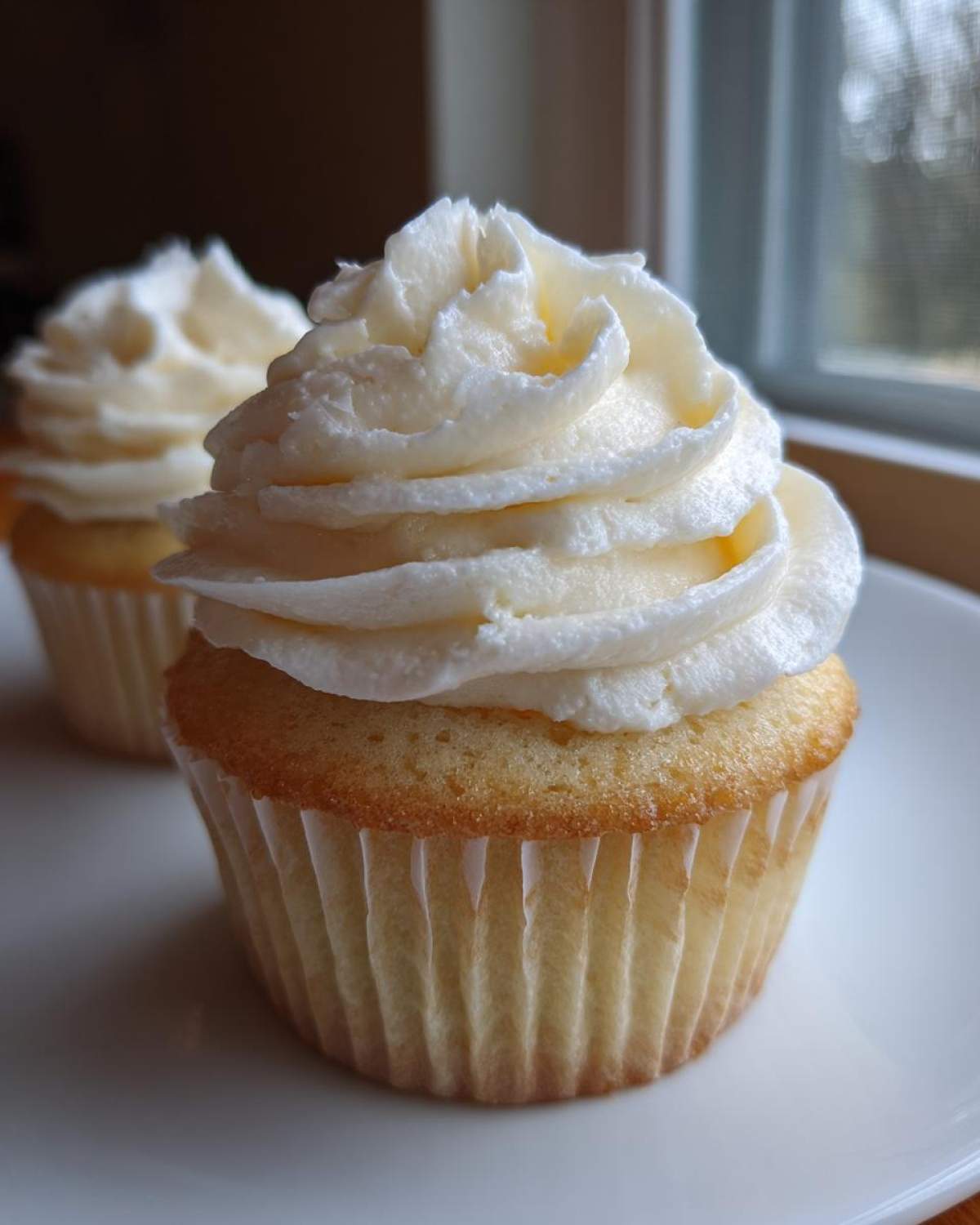 A close-up of a perfectly baked vanilla cupcake topped with a generous swirl of white vanilla frosting.