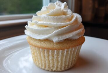 Close-up of a single, perfectly baked vanilla cupcake topped with a tall swirl of white vanilla buttercream frosting.