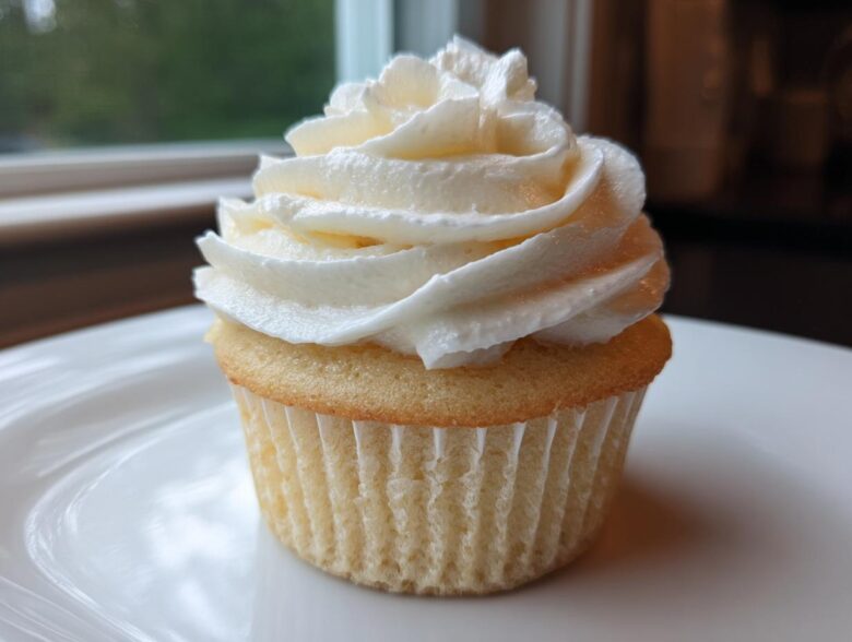 Close-up of a single, perfectly baked vanilla cupcake topped with a tall swirl of white vanilla buttercream frosting.