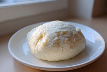 A freshly made, smooth ball of white fufu served on a small white plate, ready to eat.